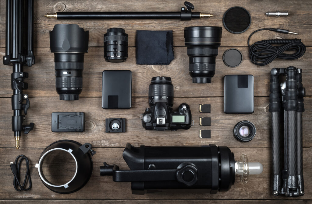 Set aus Kamera- und Fotoausrüstung (Objektiv, Stativ, Filter, Blitz, Speicherkarte, Festplatte, Reflektor) auf einem Holztisch. Hintergrund mit Zubehör für professionelle Fotografen.