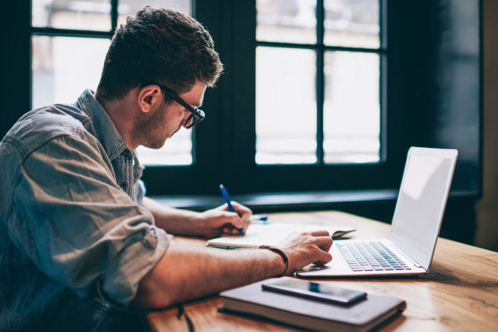 Ein junger männlicher Student (Millennial) sucht nach Informationen. Er verfasst einen Textbeitrag, um interessante Inhalte für seine eigene Website oder Webseite zu erstellen.
